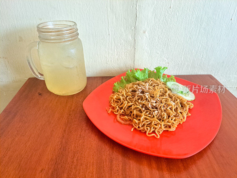 美味的炒面在一个盘子里，在杯子里加了酸橙。Mi Goreng Dan Es Jeruk Nipis。食物和饮料菜单。